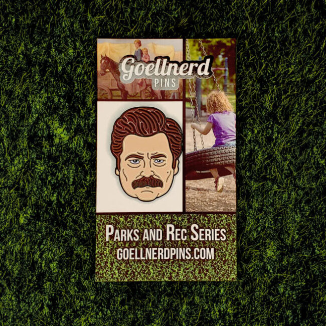 Ron Swanson Enamel Pin on a backing card in the grass